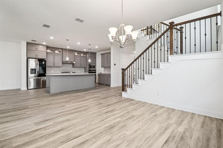 Kitchen with gray cabinets, a chandelier, light wood finished floors, open floor plan, and stainless steel appliances Kitchen with gray cabinets, a chandelier, light wood finished floors, open floor plan, and stainless steel appliances