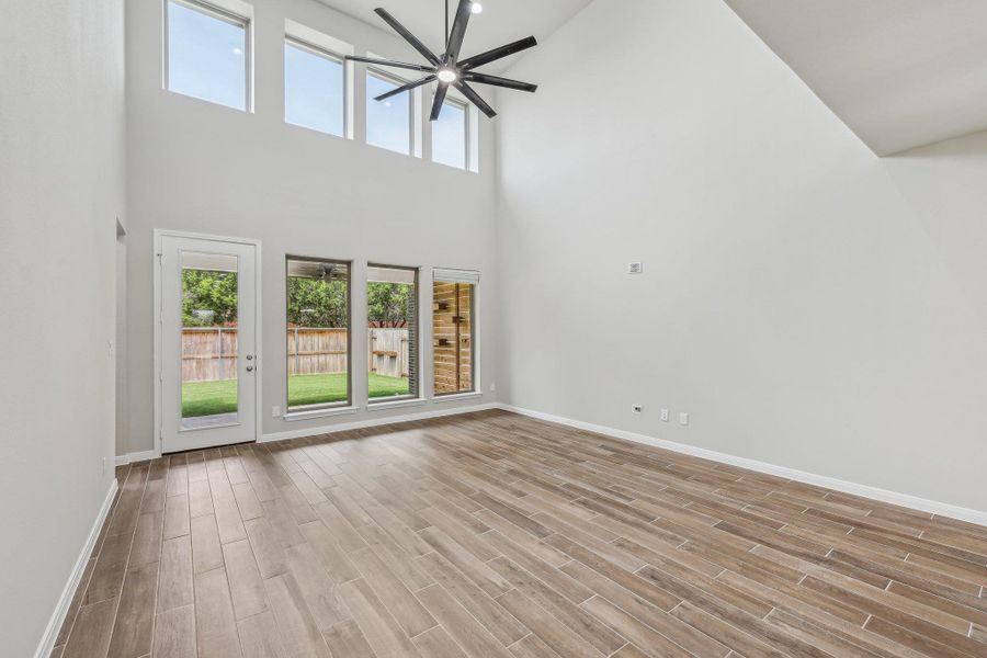 Unfurnished living room with a ceiling fan, a towering ceiling, healthy amount of natural light, baseboards, and wood finished floors Unfurnished living room with a ceiling fan, a towering ceiling, healthy amount of natural light, baseboards, and wood finished floors