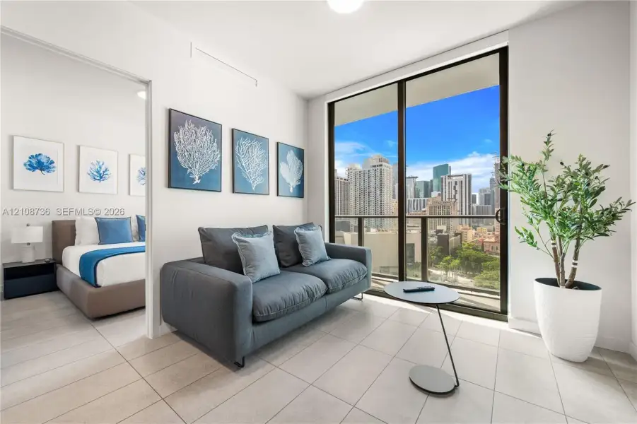 Floor-to-ceiling sliding glass doors, neutral tile flooring, and a private balcony featuring urban scenery Floor-to-ceiling sliding glass doors, neutral tile flooring, and a private balcony featuring urban scenery