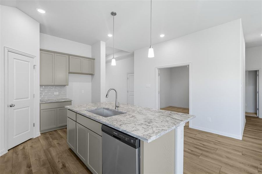Kitchen featuring stainless steel dishwasher, tasteful backsplash, hanging light fixtures, light wood-style flooring, and gray cabinets Kitchen featuring stainless steel dishwasher, tasteful backsplash, hanging light fixtures, light wood-style flooring, and gray cabinets