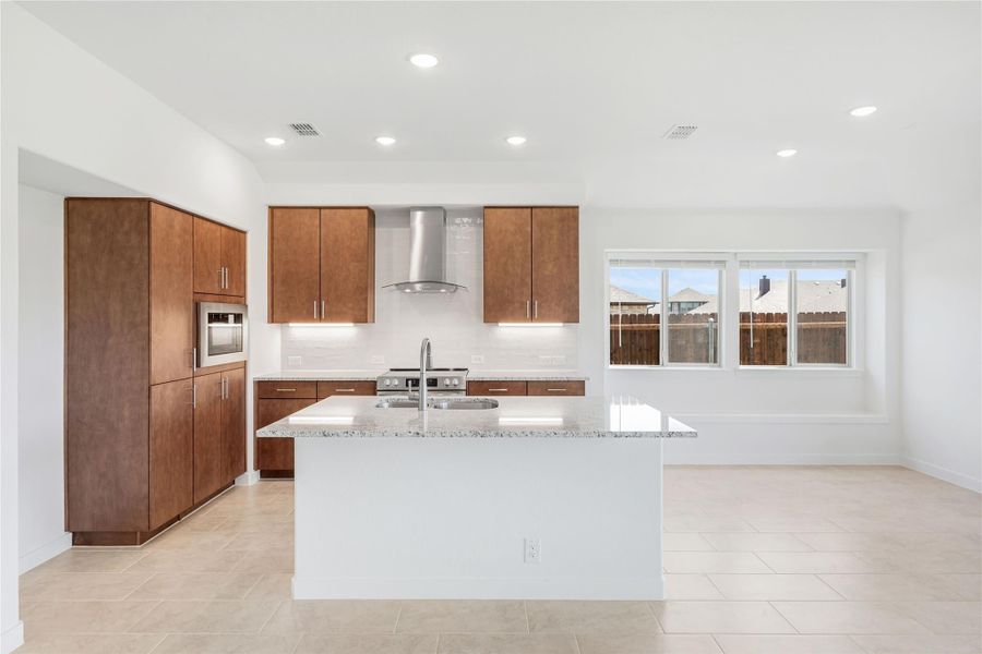 Kitchen with brown wood cabinets, granite island, stainless steel range hood, and tile floors