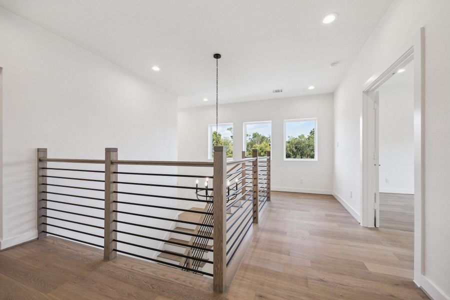 The stair landing and hallway is bright and welcoming, showcasing the beautifully crafted stair rails and bannisters. The double doorway on the right leads to the primary suite. The stair landing and hallway is bright and welcoming, showcasing the beautifully crafted stair rails and bannisters. The double doorway on the right leads to the primary suite.