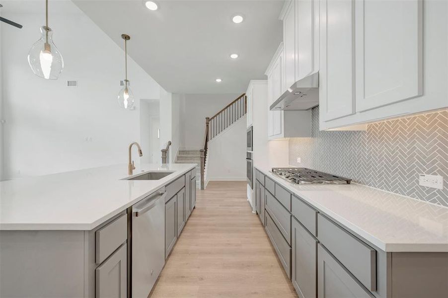 Modern kitchen featuring light gray and white cabinetry, a herringbone tile backsplash, and light-toned wood-finish flooring Modern kitchen featuring light gray and white cabinetry, a herringbone tile backsplash, and light-toned wood-finish flooring