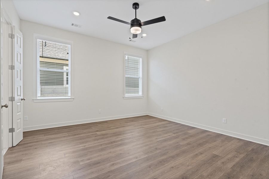 Spacious interior featuring wood-finish flooring, two windows with blinds, recessed lighting, and a ceiling fan