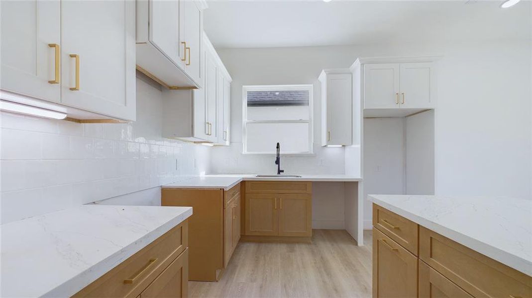 The natural wood cabinetry is thoughtfully complemented by white Calacatta quartz countertops and gold hardware. A sleek stainless steel farmhouse sink, paired with dark plumbing hardware, adds a modern, sophisticated touch to the space.