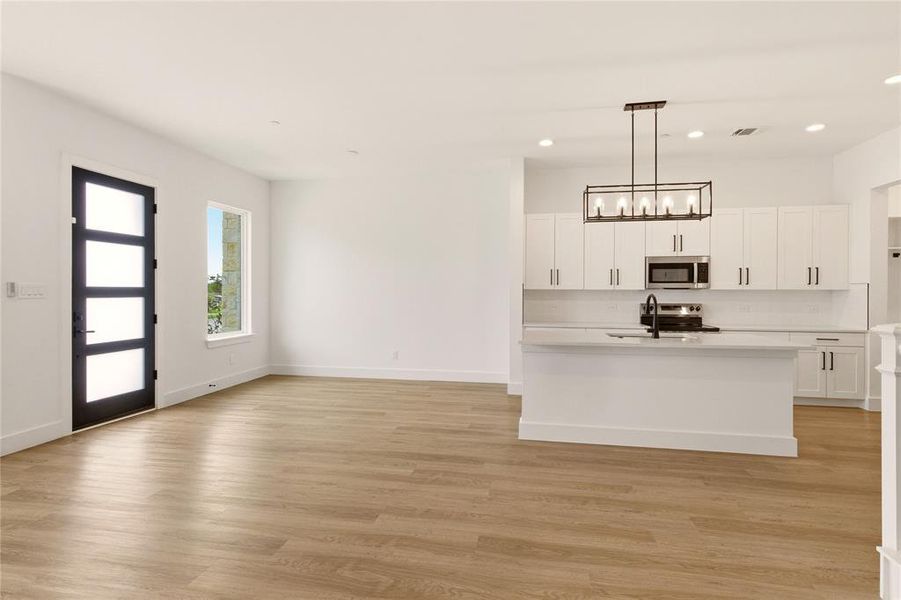 Kitchen featuring white cabinets, light wood-style flooring, stainless steel microwave, hanging light fixtures, and electric stove