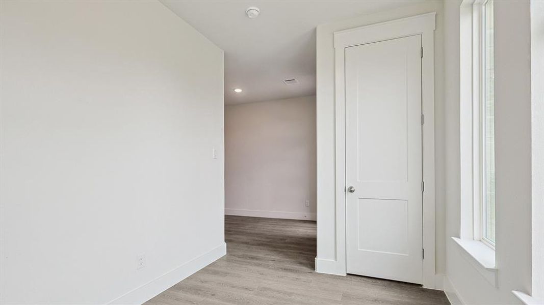 Light-filled interior space featuring wood-finish flooring, white trim, recessed lighting, and a two-panel door
