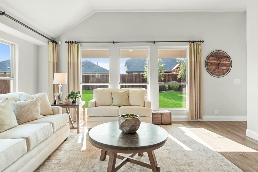Living room with vaulted ceiling, hardwood floors, cream sofas, and large windows overlooking a backyard