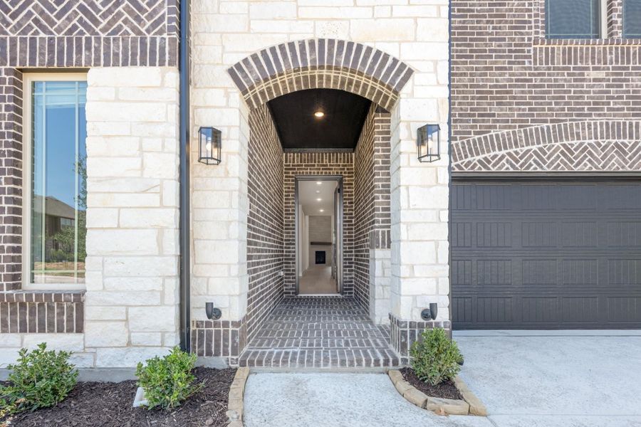 Home entrance with arched brick and stone surround, wall sconces, and covered entryway leading to front door