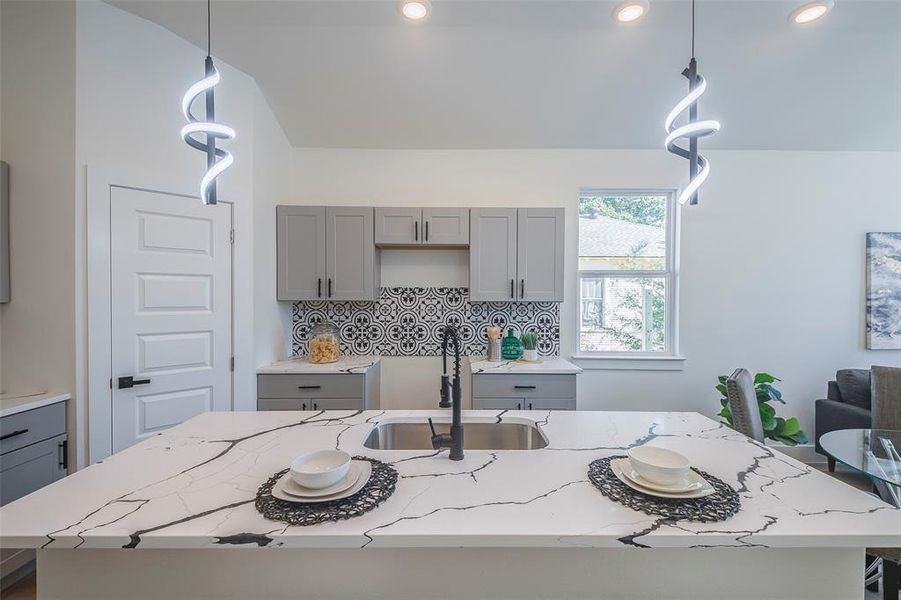 Kitchen with gray cabinetry, a center island with sink, sink, decorative backsplash, and decorative light fixtures