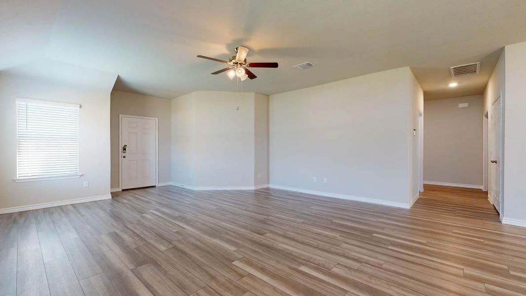 Spacious open-concept living area featuring wood-finish flooring, neutral wall tones, a ceiling fan with integrated lighting, a window with blinds, and recessed lighting in the hallway