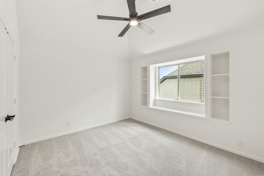 Empty bedroom with carpet, ceiling fan, built-in shelves flanking a center window Empty bedroom with carpet, ceiling fan, built-in shelves flanking a center window