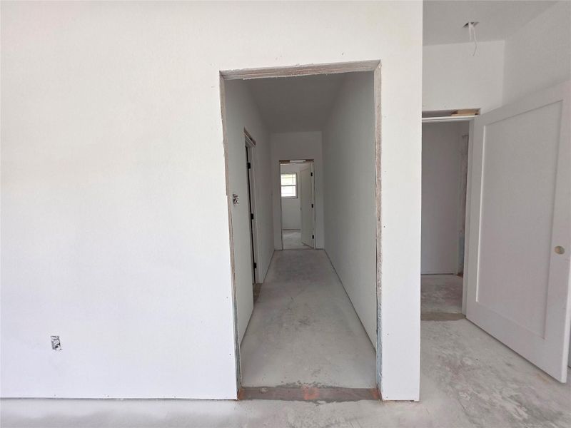 Unfinished interior hallway featuring bare concrete flooring and white primed walls, with an open doorway leading to another room