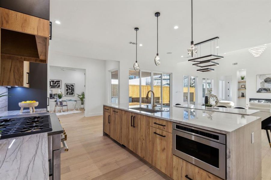 Kitchen featuring sink, light stone countertops, light hardwood / wood-style floors, decorative light fixtures, and a large island with sink