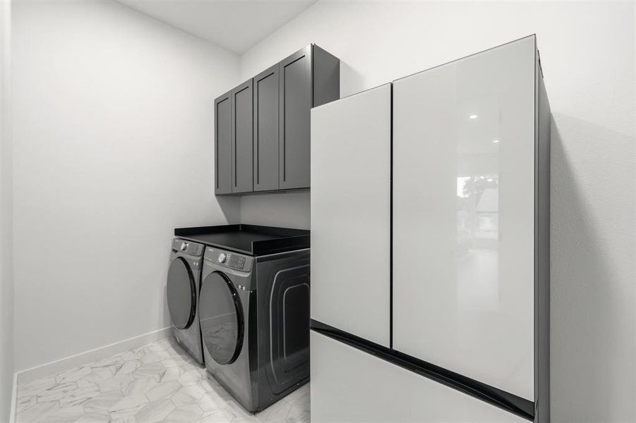 Laundry area featuring light marble finish floors, washer and dryer, and cabinet space