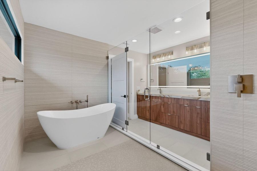 A spacious primary bathroom boasts a freestanding soaking tub and a sleek dual vanity behind a glass shower enclosure.