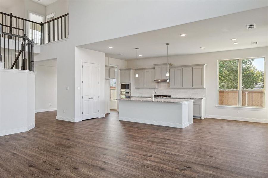 Kitchen featuring gray cabinetry, light stone countertops, decorative light fixtures, dark hardwood / wood-style flooring, and a kitchen island with sink