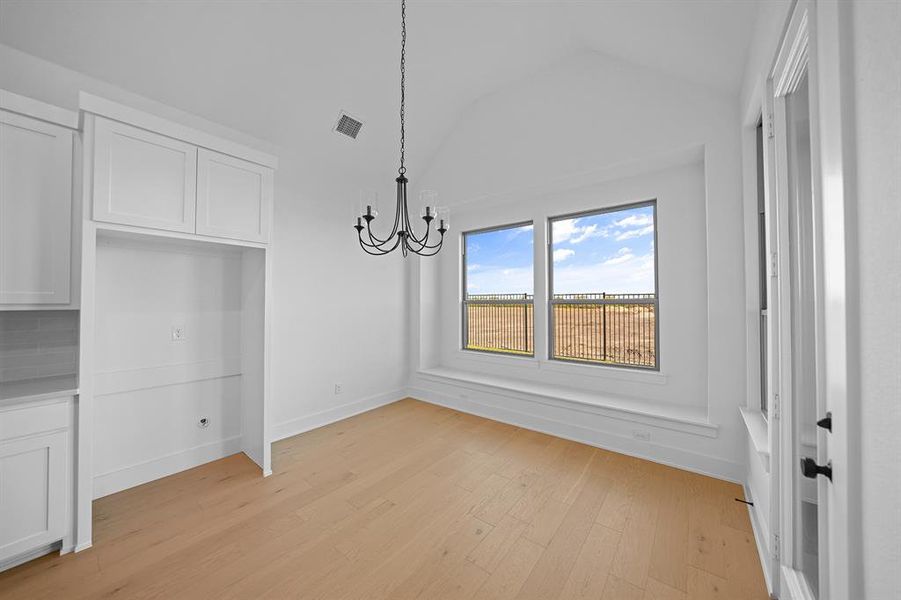 Unfurnished dining area with lofted ceiling, light wood finished floors, and a chandelier