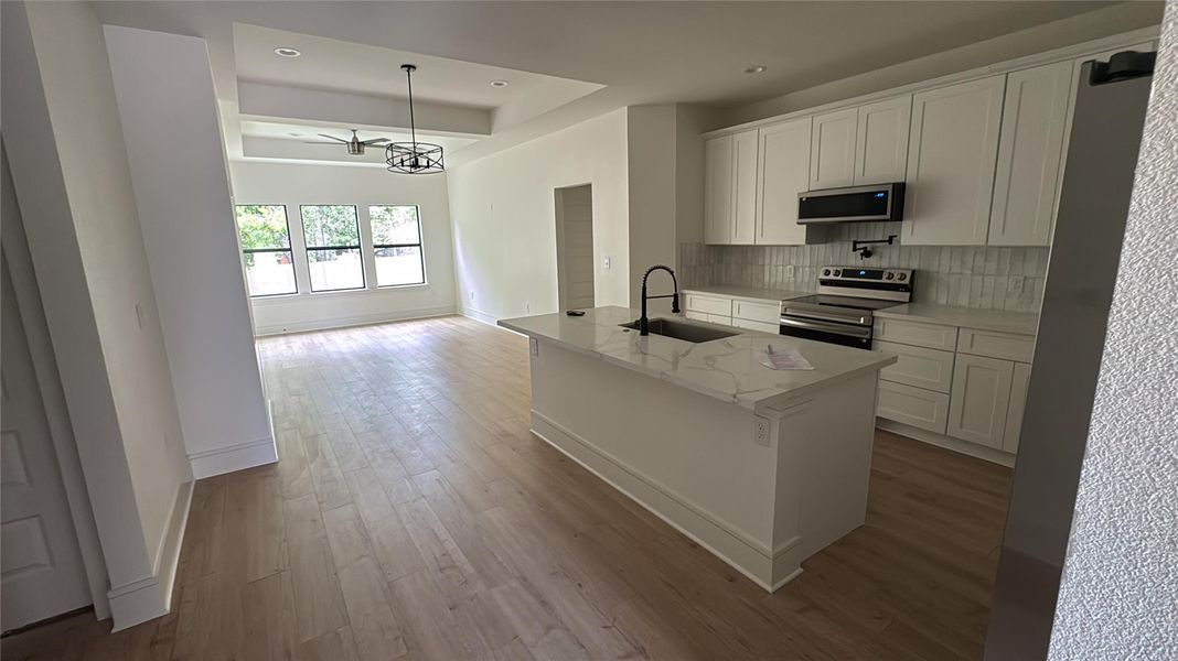 Kitchen featuring white cabinetry, appliances with stainless steel finishes, light wood finished floors, an island with sink, and recessed lighting