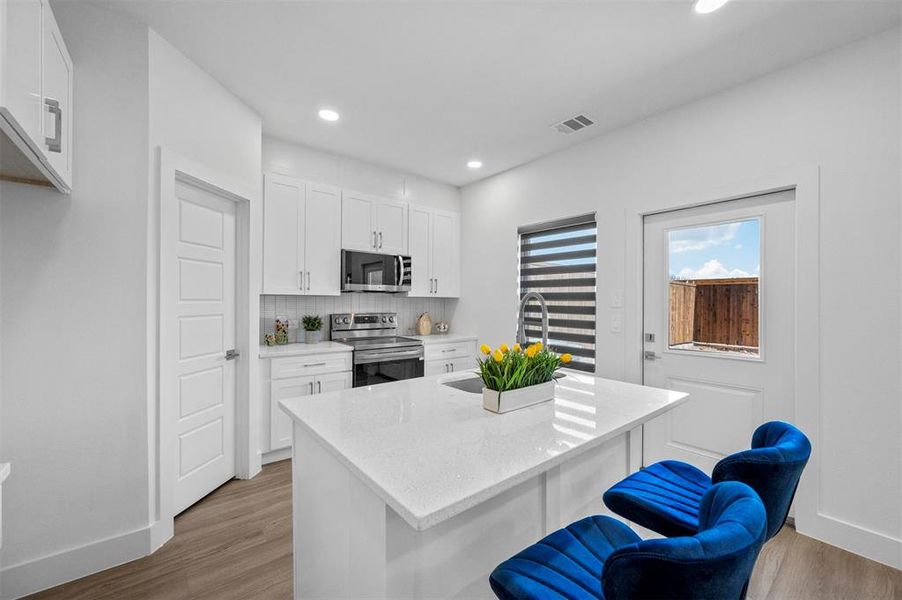 Kitchen featuring a center island, visible vents, appliances with stainless steel finishes, white cabinets, and a kitchen breakfast bar