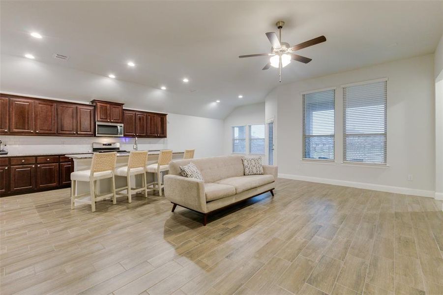 Living room with lofted ceiling, ceiling fan, and light wood-type flooring