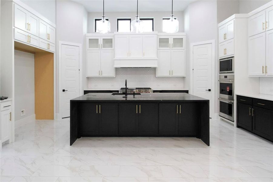 Kitchen featuring appliances with stainless steel finishes, white cabinetry, an island with sink, and hanging light fixtures