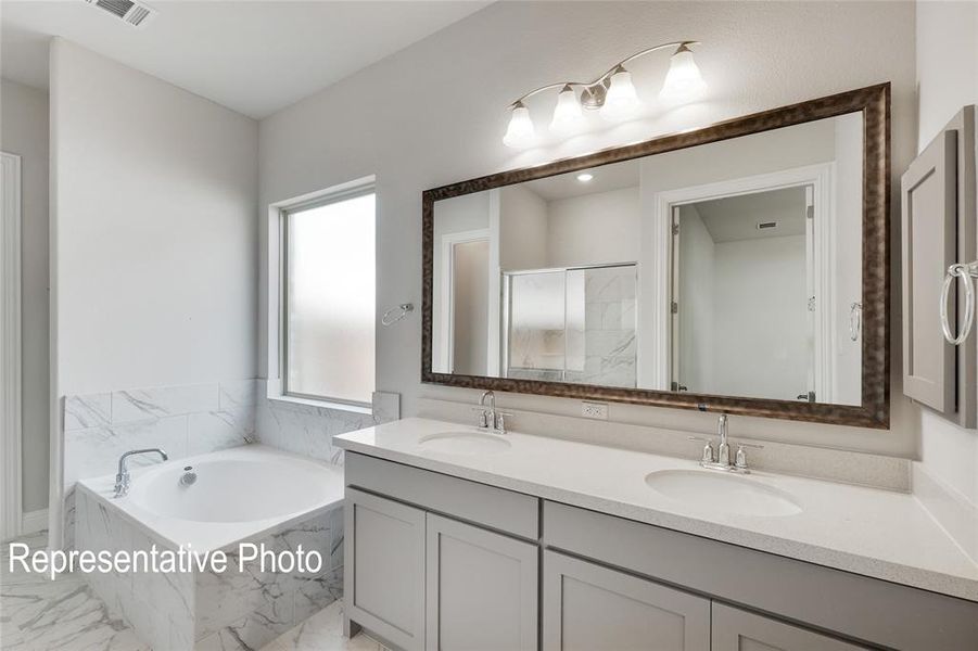 Bathroom featuring a wealth of natural light, a relaxing tiled bath, dual vanity, and tile flooring