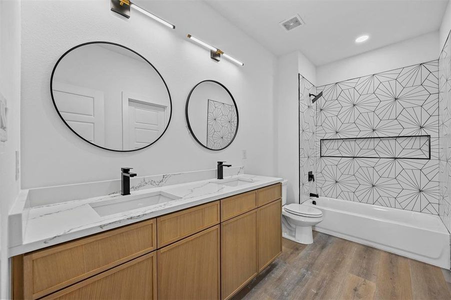 Full bathroom with double sink vanity, tiled shower / bath combo, toilet, and hardwood / wood-style floors