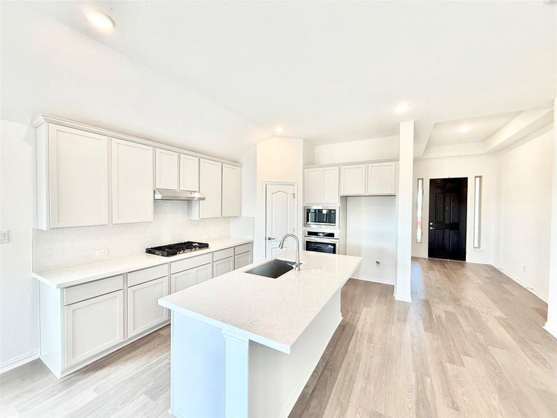 Kitchen with recessed lighting, white cabinets, light wood finished floors, tasteful backsplash, and a kitchen island with sink