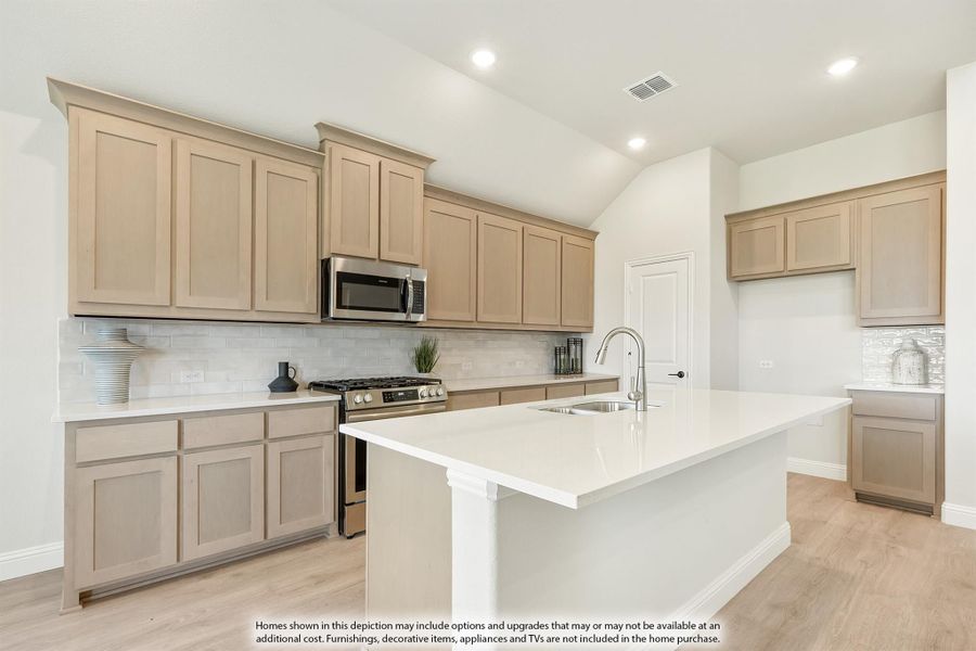 Kitchen with light wood cabinets, white island with sink, stainless steel appliances, and subway tile backsplash