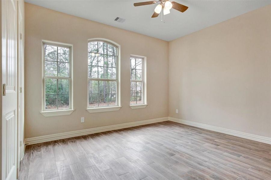This front bedroom features three large windows that provide plenty of natural light, neutral-colored walls, wood-look tile flooring, and a ceiling fan, This front bedroom features three large windows that provide plenty of natural light, neutral-colored walls, wood-look tile flooring, and a ceiling fan,