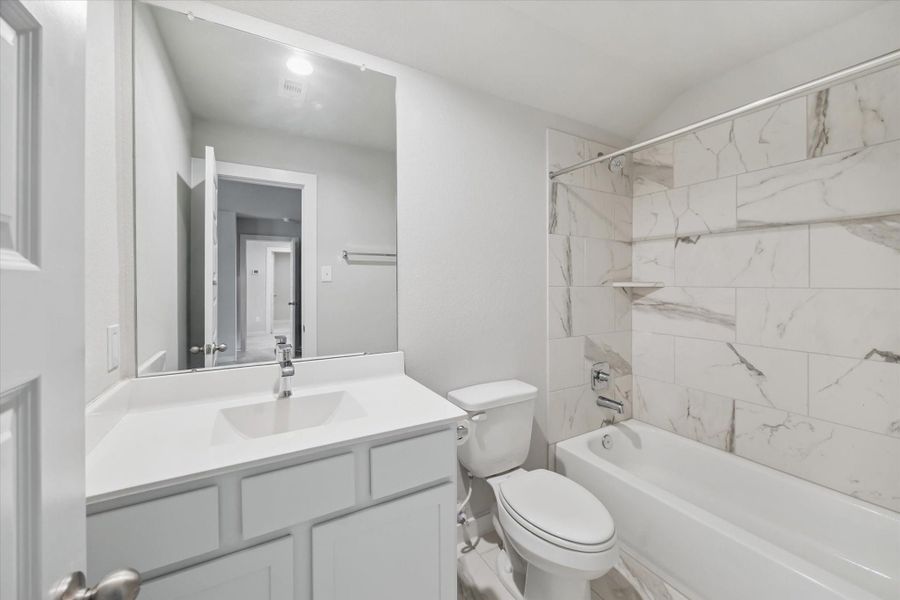 This en-suite bathroom features a modern design with a white vanity, polished countertop, and a large mirror. The bathtub is complemented by elegant marble-style tile, creating a bright and clean atmosphere. This en-suite bathroom features a modern design with a white vanity, polished countertop, and a large mirror. The bathtub is complemented by elegant marble-style tile, creating a bright and clean atmosphere.