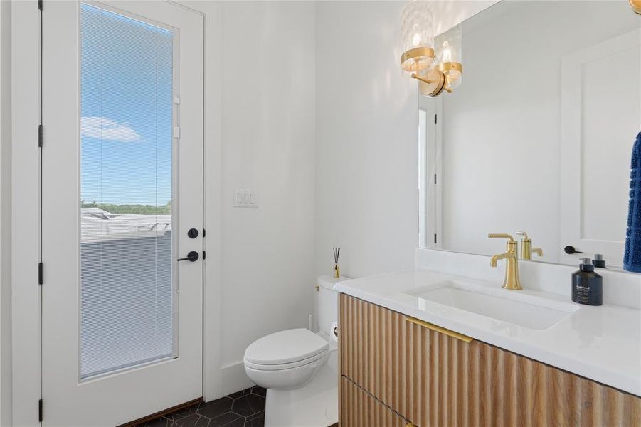 Bathroom featuring a full-light door, hexagonal floor tiles, a white toilet, and a vanity with a fluted wood-finish front, white countertop, integrated sink, and gold-finish faucet