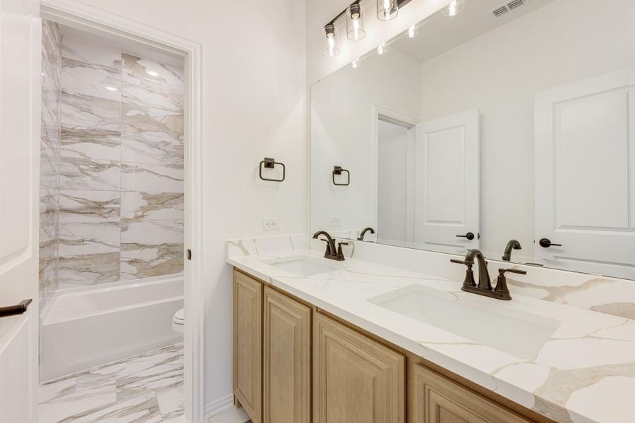 Bathroom with double sink vanity, marble countertops, and tub-shower with marble tile surround Bathroom with double sink vanity, marble countertops, and tub-shower with marble tile surround