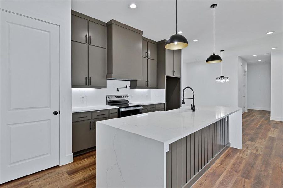 Kitchen with gray cabinets, stainless steel electric range, a kitchen island with sink, light stone counters, and pendant lighting