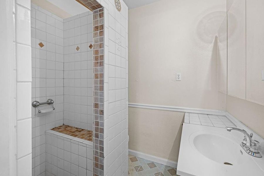 Full bath featuring tiled shower, vanity, and light tile patterned floors