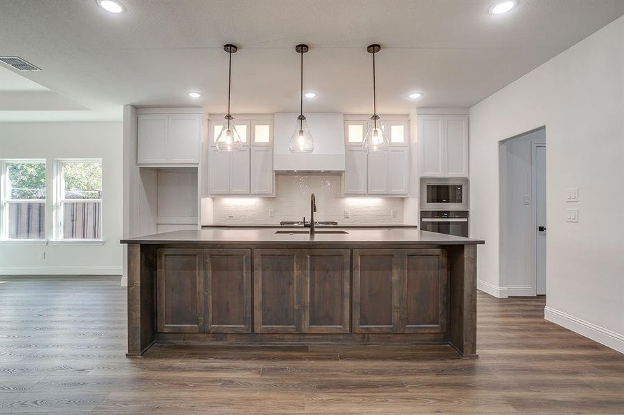 Kitchen with white cabinets, custom range hood, appliances with stainless steel finishes, hanging light fixtures, and dark brown cabinetry
