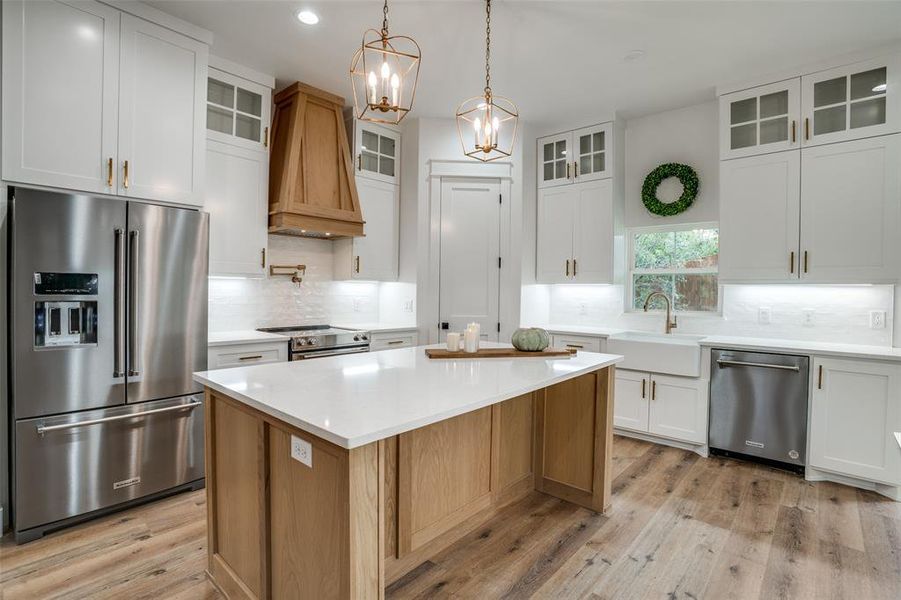 Kitchen with sink, white cabinets, appliances with stainless steel finishes, a kitchen island, and custom exhaust hood