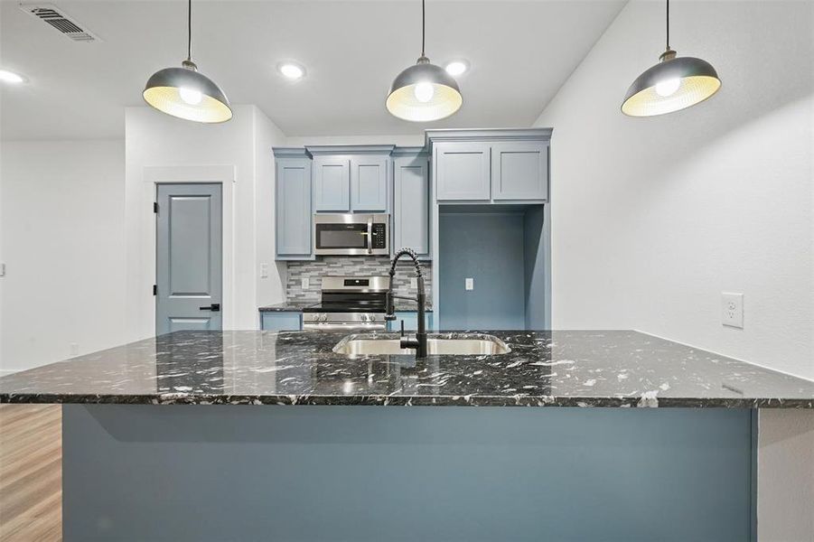 Kitchen featuring dark stone counters, visible vents, appliances with stainless steel finishes, a sink, and backsplash