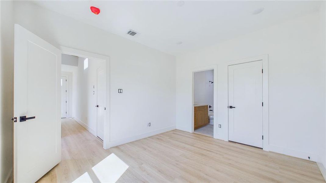 The spacious first-floor bedroom showcases wood-like LVP flooring, recessed lighting, and a large window that bathes the room in natural light.