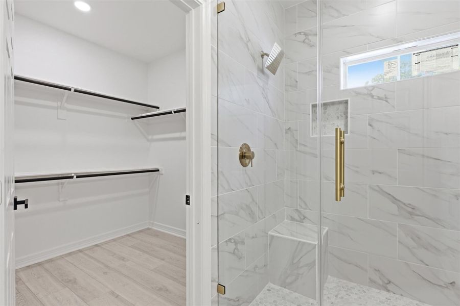 Primary bathroom walk in shower with frameless glass door, gold hardware, and floor to ceiling marble look tile.