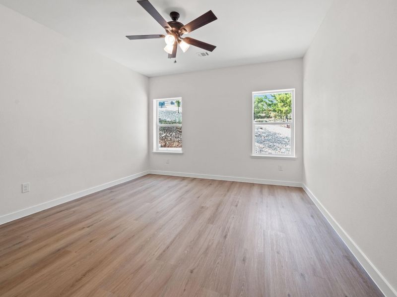 Bright room featuring wood-finish flooring, two windows, and a ceiling fan with integrated lighting