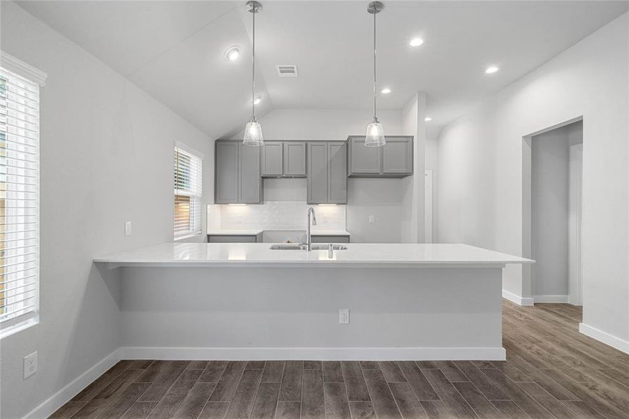 This stunning kitchen displays such a beautiful contrast with the grey cabinets, custom neutral paint, Quartz countertops, light modern backsplash, oversized kitchen peninsula with extra storage, breakfast bar, recessed lighting with additional pendant lighting, high ceilings.