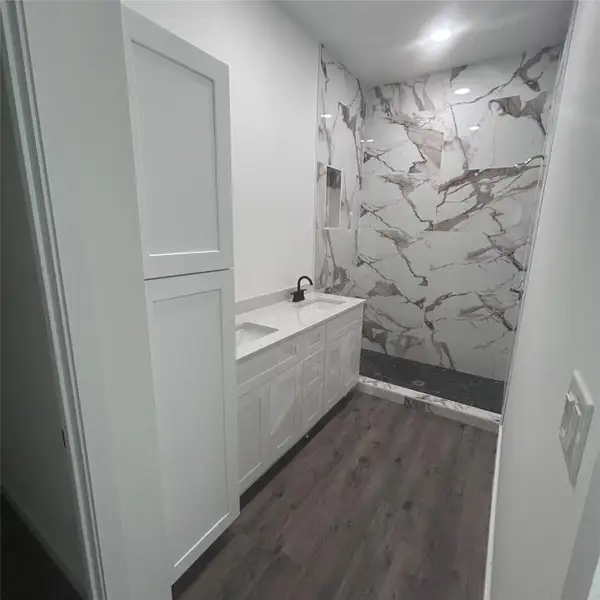 Bathroom with a marble finish shower, double vanity, and dark wood finished floors Bathroom with a marble finish shower, double vanity, and dark wood finished floors