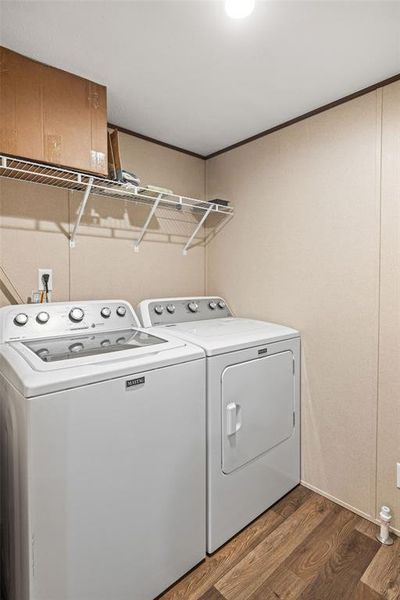 Dedicated laundry area featuring wood-finish flooring, light-toned wall paneling, and a convenient overhead wire shelving system Dedicated laundry area featuring wood-finish flooring, light-toned wall paneling, and a convenient overhead wire shelving system
