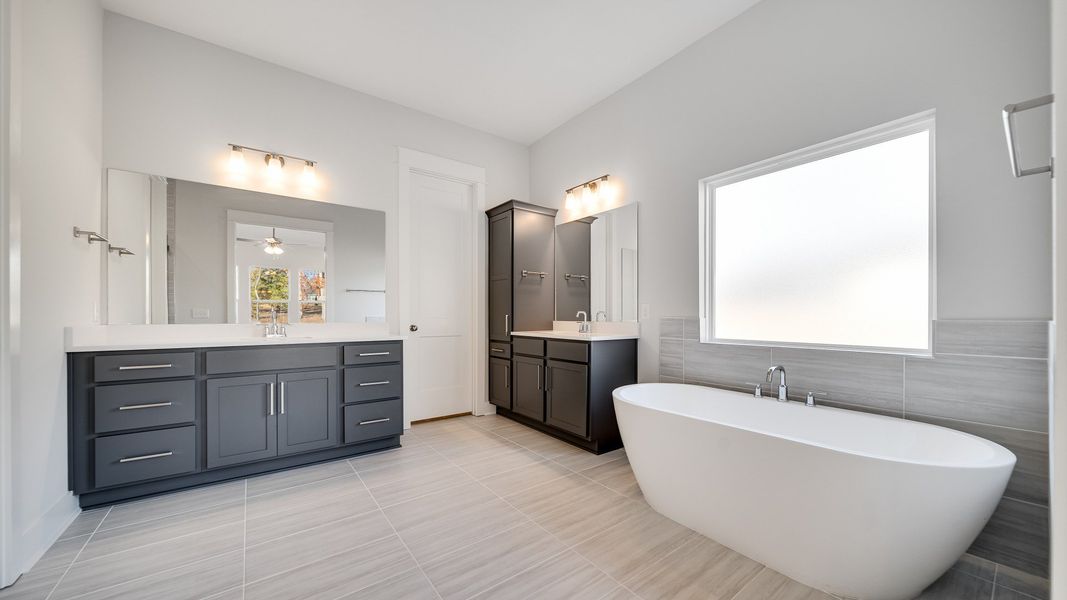 Large tiled bathroom with multiple vanities, glass shower enclosure, and freestanding tub