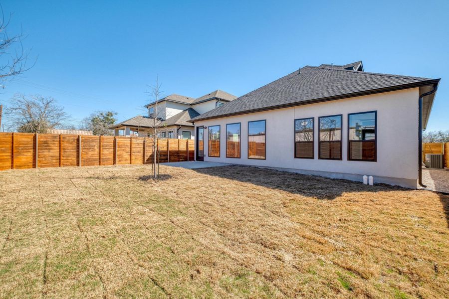 Back of house featuring a yard, central AC, stucco siding, and fence