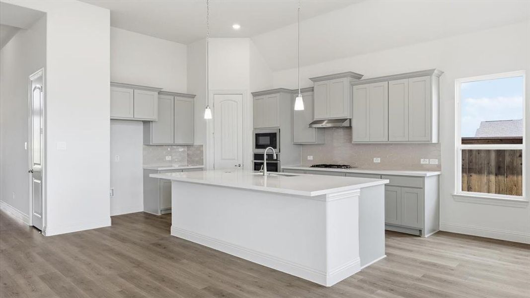 Open-concept kitchen featuring an oversized island, light gray cabinetry, built-in stainless steel appliances, and wood-finish flooring