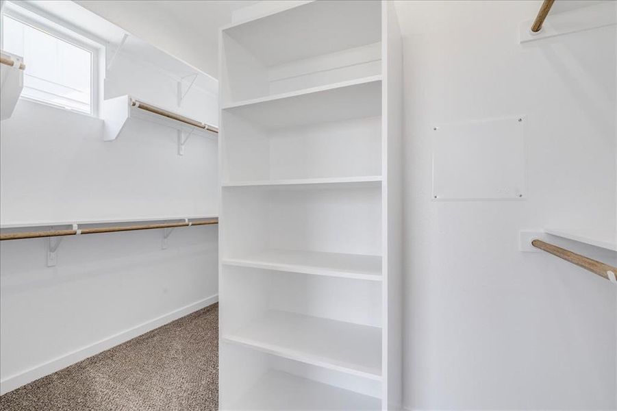 A well-lit primary walk-in closet offers ample storage with shelving and hanging rods. A well-lit primary walk-in closet offers ample storage with shelving and hanging rods.