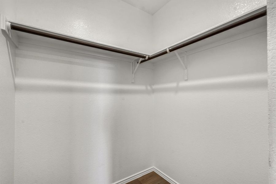 A spacious walk-in closet features built-in shelving, hanging rods, and wood-look flooring. A spacious walk-in closet features built-in shelving, hanging rods, and wood-look flooring.